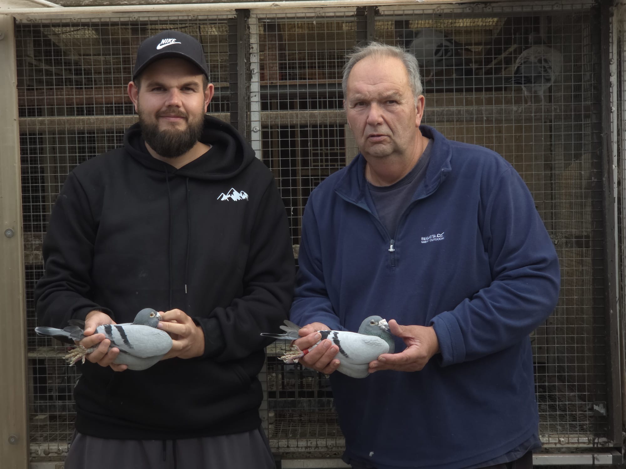 Two fanciers holding racing pigeons in front of their loft